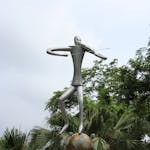 Modern sculpture of a violinist on a globe surrounded by lush greenery outdoors.